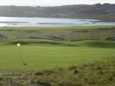 Golfgrün mit Markierungsfahne und Meeresblick auf dem  Narin und Portnoo Golfplatz in Irland
