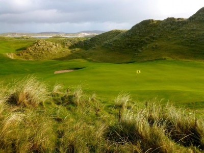 Golfgrün mit Markierungsfahne und Meeresblick auf dem  Narin und Portnoo Golfplatz in Irland